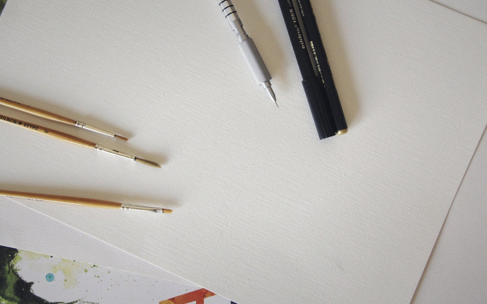 Paintbrushes, mechanical pencil, and pen resting on blank textured paper